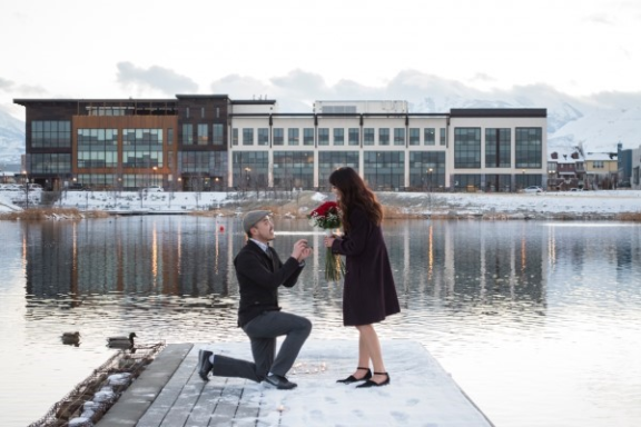 Man proposes to woman with roses on a dock.