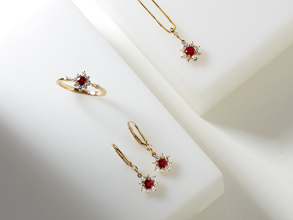 Yellow gold ruby and diamond cluster necklace, ring and dangle earrings on white background.