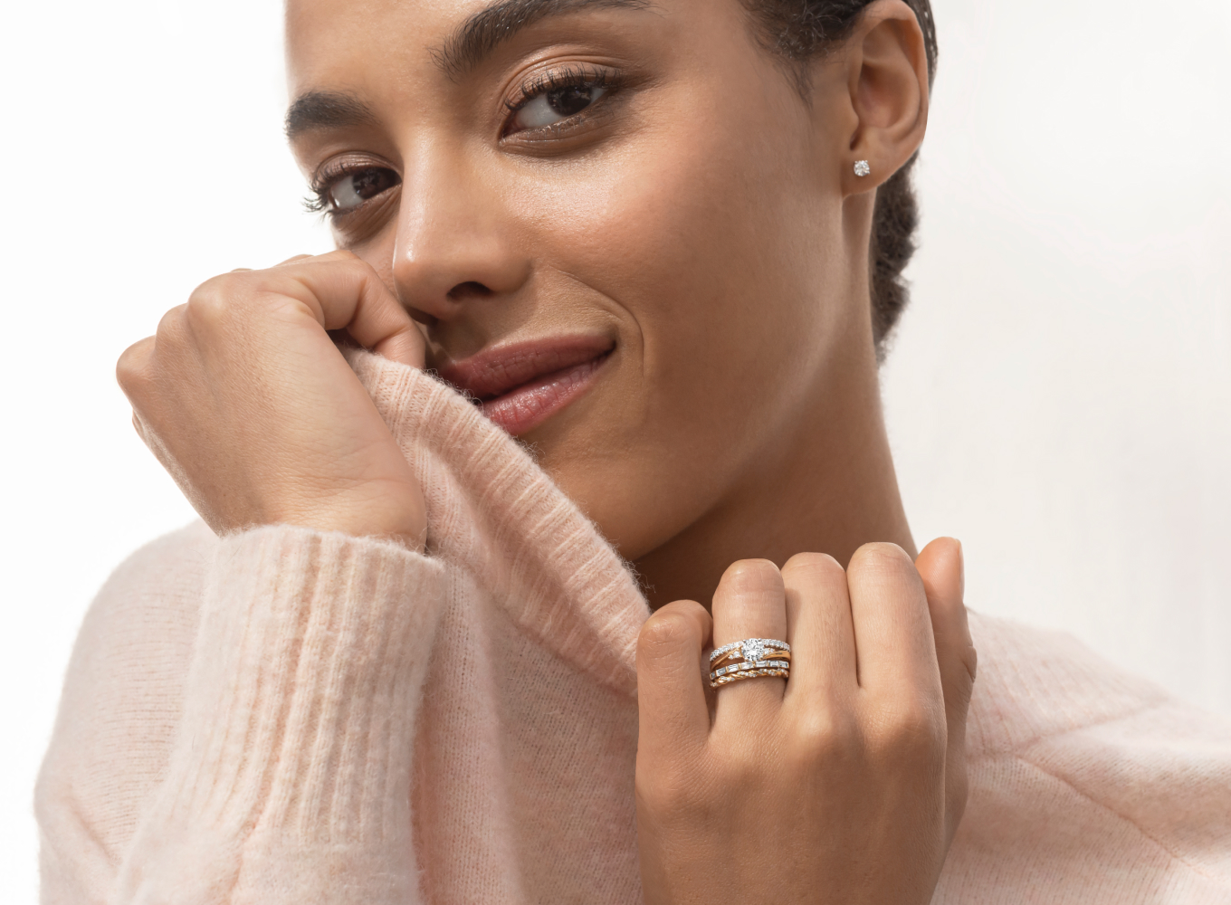 woman in a sweater wearing stackable rings. From top to bottom: Faye Pave-Set Diamond Wedding Band in 14k White Gold Crafted in quality 14 karat white gold, fifteen round natural diamonds, at approximately .20 carat total weight, are hand-matched for exceptional fire and sparkle. This 1.5mm band with delicate pave design offers a spectacular finishing touch. Plume Engagement Ring Natural diamond accents and stunning milgrain detail will embrace the center stone of your dreams in this beautiful, vintage-inspired engagement ring. Crafted in warm 14-karat yellow gold, it features an ornate design along the profile with additional milgrain detail. For more information on selecting your center stone, live chat online, call a customer service representative at 1-866-467-4263, or visit one of our store locations. Avra Diamond Band Baguette natural diamond accents line this beautiful band in a nod back to the glamorous Art Deco era. Crafted in warm 14-karat yellow gold, all the diamonds are hand matched for consistent color, clarity, and sparkle. Diamond Twist Band Thirty round natural diamonds, at approximately .13 carat total weight, give this elegant 1.5mm swirl band radiance. These exquisite, hand-matched stones are set in the quality 14 karat yellow gold. 