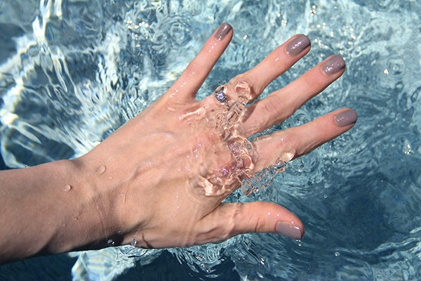 Woman holding her hand underwater while wearing engagement ring.