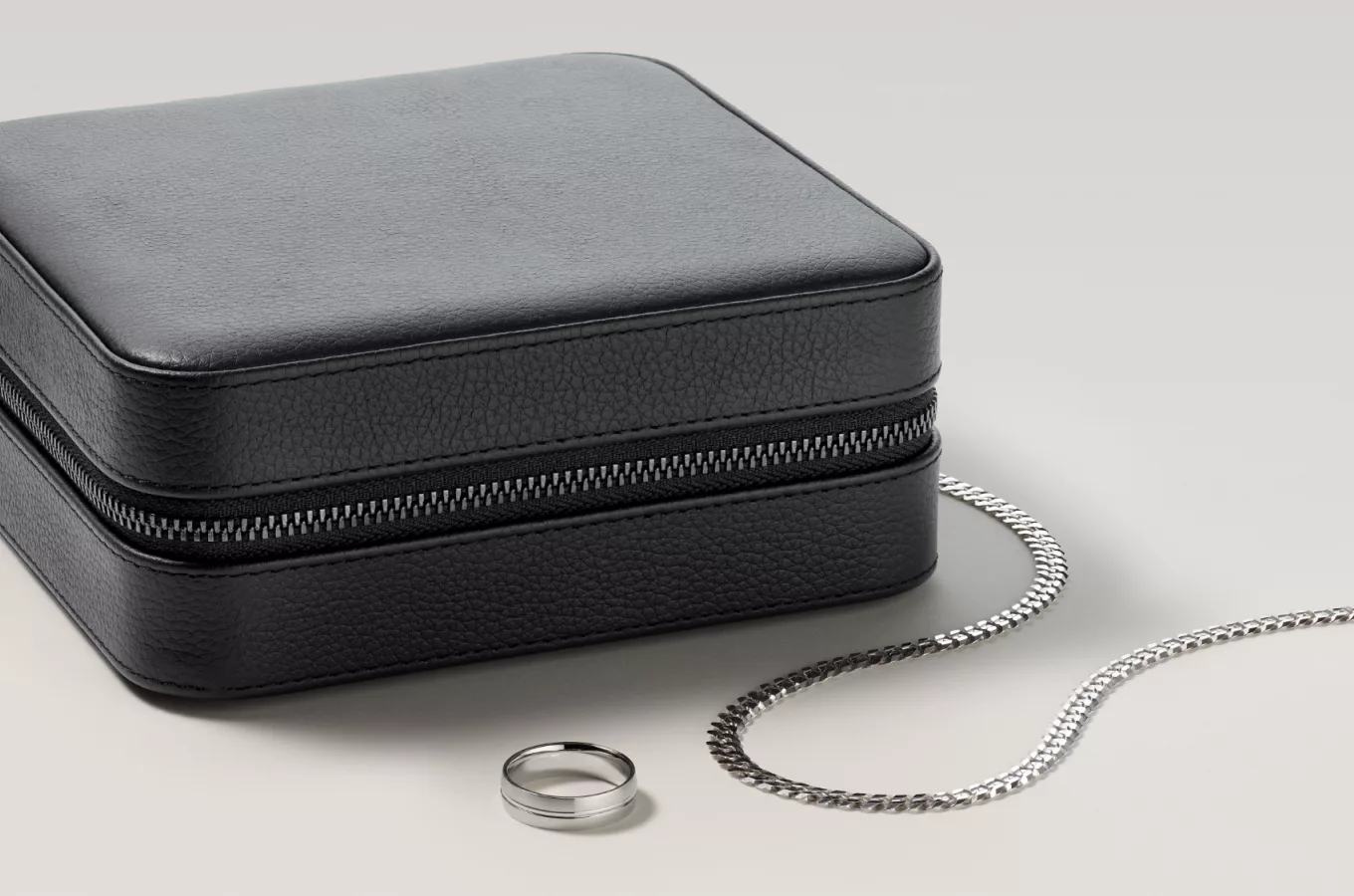 mens white gold chain and white gold wedding band next to a black leather jewelry case. Medium Leather Jewelry Case
Whether traveling from work to the gym, or tagging along in your carry-on, this leather jewelry case is the perfect way to organize and protect your fine jewelry collection every day. It features a stylish black pebbled leather exterior and a soft suede interior with various compartments, including a detachable earring bar, ring rolls, and enough space for bangle bracelets and watches. 24 in Mens Miami Cuban Chain in Sterling Silver (8mm)This bold sterling silver chain will be sure to capture attention. Twenty-four inches in length, this Miami Cuban chain is secured by a lobster clasp and a high polished finish adding subtle flair to the 8mm wide design. Contemporary Wedding Band in Tantalum (7mm)
This tantalum wedding band is hypoallergenic, making it perfect for someone with sensitive skin, and will resist scratching and corrosion.
