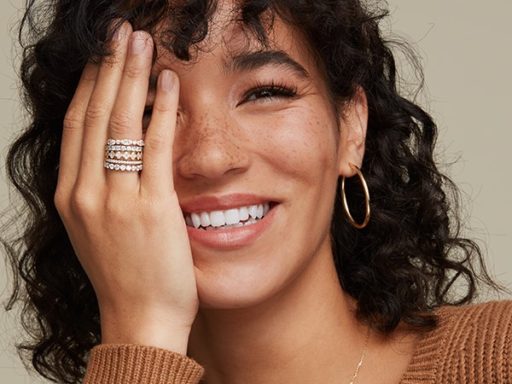 Woman wearing stacked rings and gold hoop earrings.