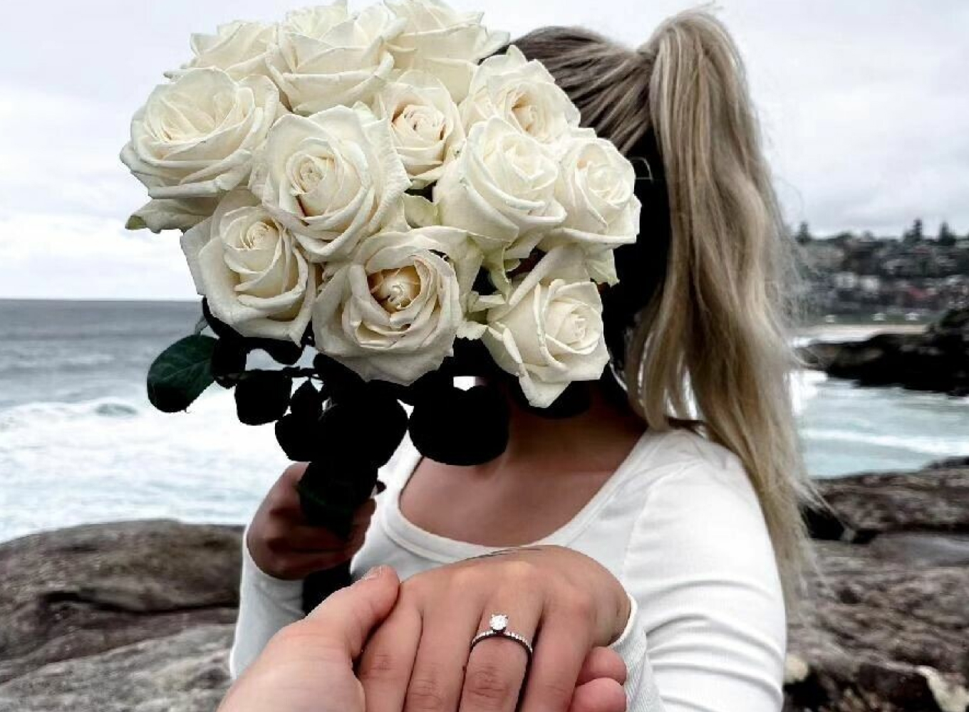 Woman hiding behind roses holding engagement ring after being proposed to
