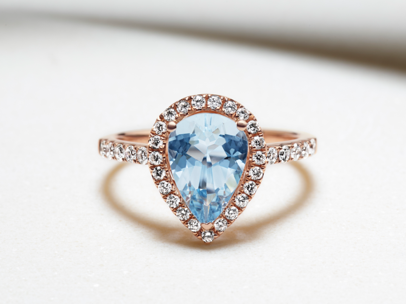 rose gold ring with pear shaped aquamarine center stone, pave band, and halo setting