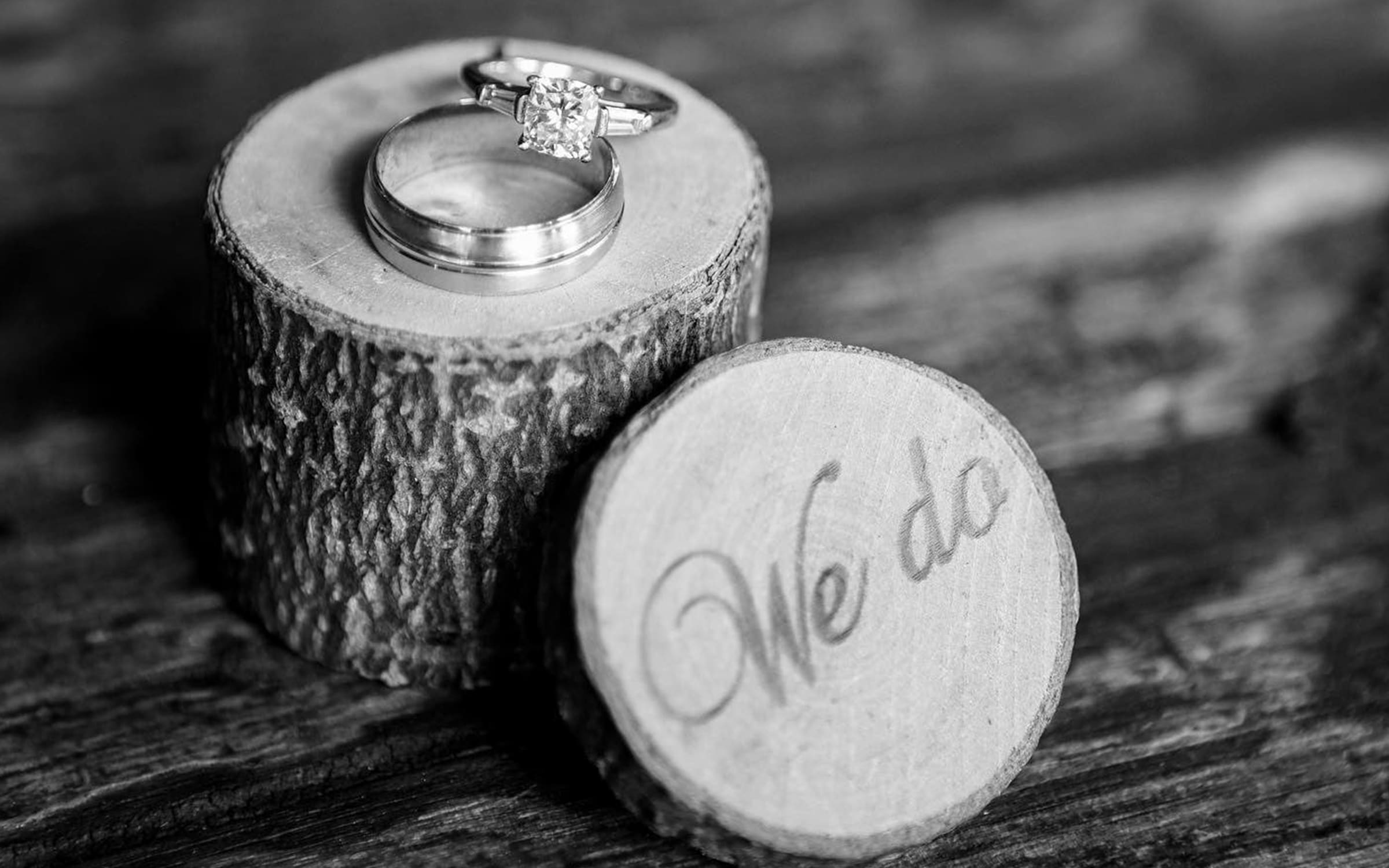 wedding rings stacked on a wood pedestal engraved with "We Do"