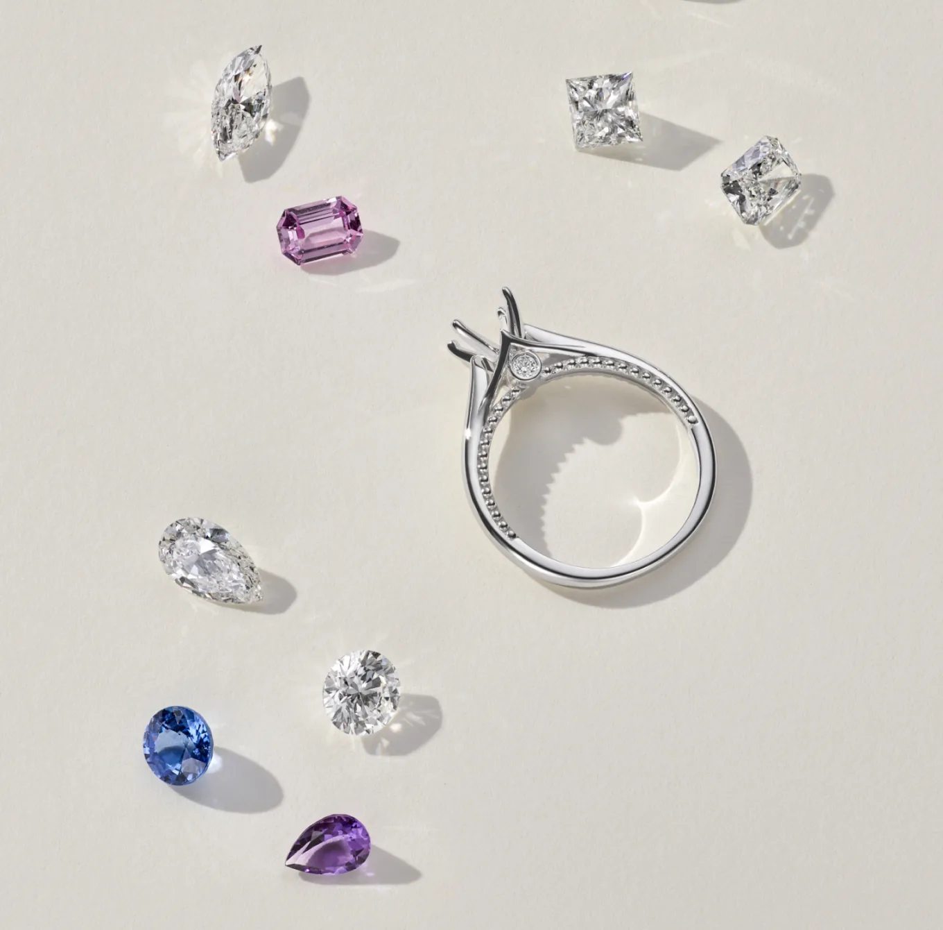 In the center of the image is a solitaire engagement ring. It has a white gold band and a single, round diamond in a prong setting. The diamond is likely cut in a brilliant round cut, which is the most popular cut for diamonds because it maximizes sparkle. Scattered around the engagement ring are several loose diamonds. These diamonds vary in size and may be used to create a custom engagement ring.

Hidden Milgrain Engagement Ring
This sleek 14-karat white gold engagement ring features a simple top-down view with ornate details hidden along the sides. Milgrain lines the profile, giving way to a natural diamond accent on either side of the setting. Add the center stone of your dreams to complete this elegant design. For more information on selecting your center stone, Live Chat online, call a customer service representative at 1-866-467-4263, or visit one of our store locations.