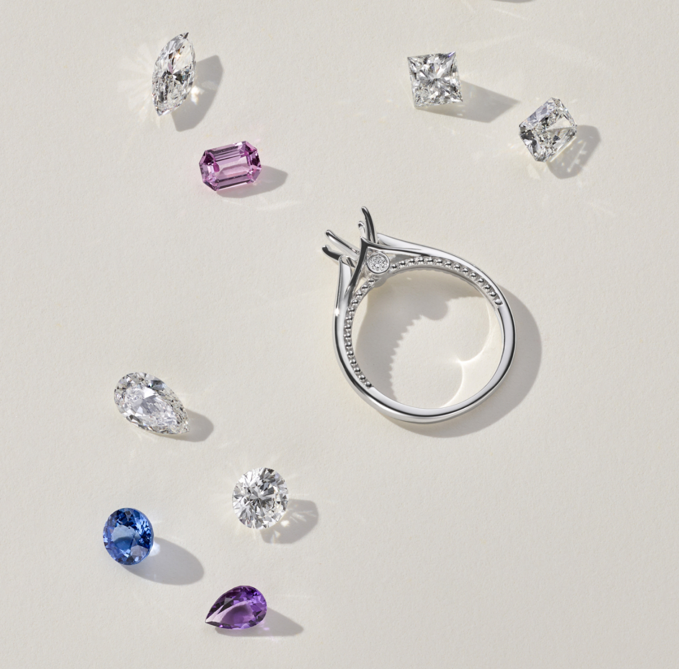 In the center of the image is a solitaire engagement ring. It has a white gold band and a single, round diamond in a prong setting. The diamond is likely cut in a brilliant round cut, which is the most popular cut for diamonds because it maximizes sparkle. Scattered around the engagement ring are several loose diamonds. These diamonds vary in size and may be used to create a custom engagement ring.

Hidden Milgrain Engagement Ring
This sleek 14-karat white gold engagement ring features a simple top-down view with ornate details hidden along the sides. Milgrain lines the profile, giving way to a natural diamond accent on either side of the setting. Add the center stone of your dreams to complete this elegant design. For more information on selecting your center stone, Live Chat online, call a customer service representative at 1-866-467-4263, or visit one of our store locations.