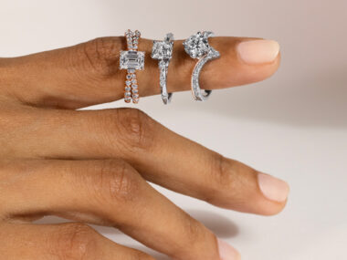 The image you sent me shows a close-up of a woman’s left hand wearing three rings. The rings are all on the ring finger. The ring closest to her knuckle is a split, rose gold band with a textured surface. The middle ring is a thin, platinum band set with a single diamond. The ring closest to her fingertip is a thicker band made of white gold. It has a large, round gemstone in the center that could be a diamond or another clear stone.