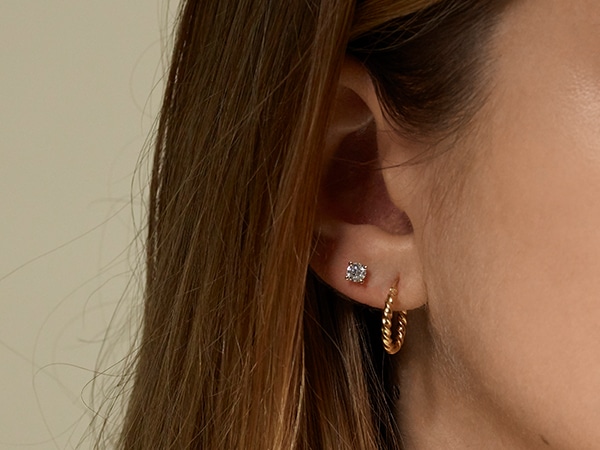 Woman wearing a gold hoop earring and a diamond stud earring.