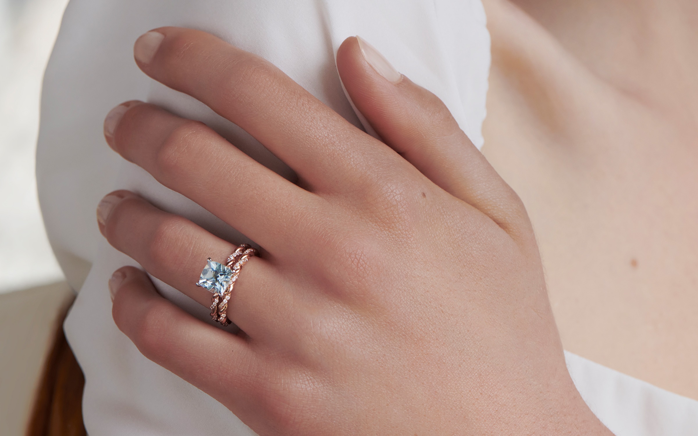 Woman wearing aquamarine engagement ring with rose gold wedding band.