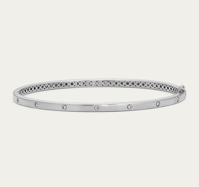 Diamond Bangle Bracelet (7.5 in). 7 round natural diamonds at approx. 0.15 tcw.  Hinged bangle design. 7.5-inch length. Approx. 3mm width. Tongue clasp & safety lock. Rhodium-plated 14k white gold