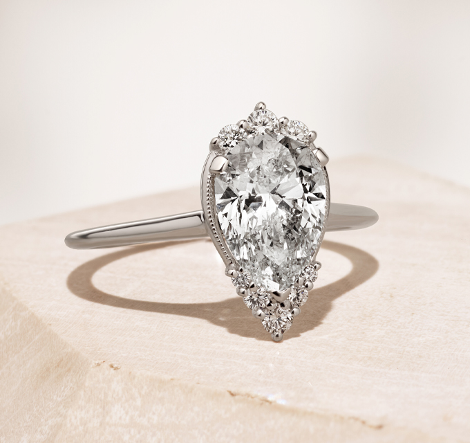 Dewdrop Diamond Pear-Shaped Engagement Ring in 14k White Gold. Center gemstone beautifully featured in this stunning halo setting. The accenting natural diamonds are strong enough to be worn every day. This halo design will make your center gemstone appear larger and keep it securely in place. 14k white gold, 8 round accenting natural diamonds at approx. 0.15 tcw, 1mm band width, Engravable and resizable