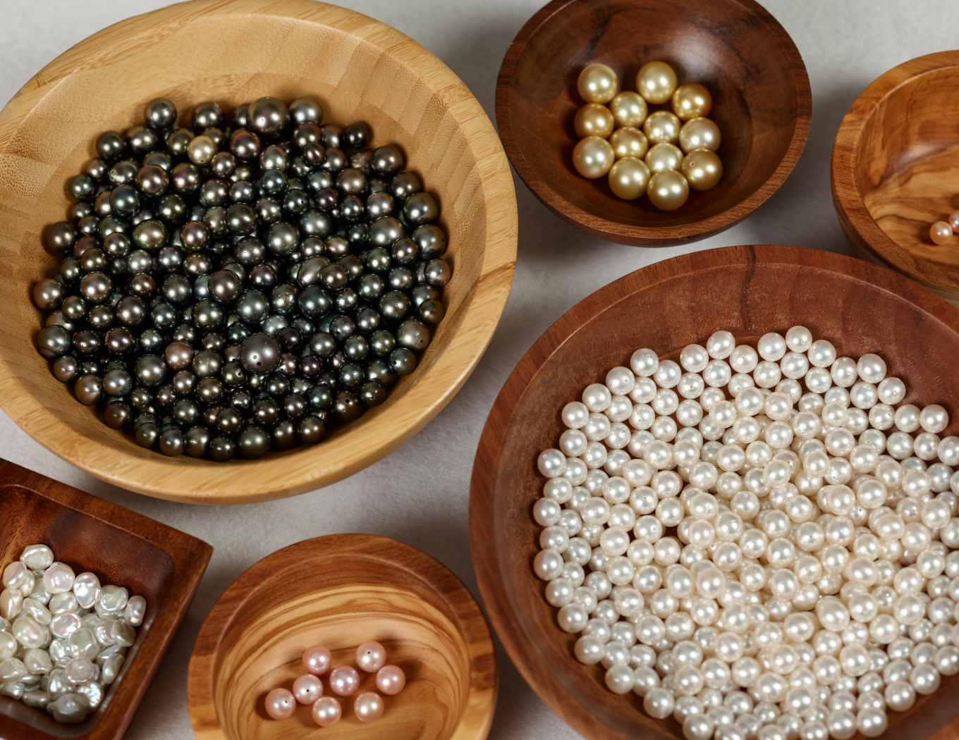 assorted pearls grouped by color in wooden bowls