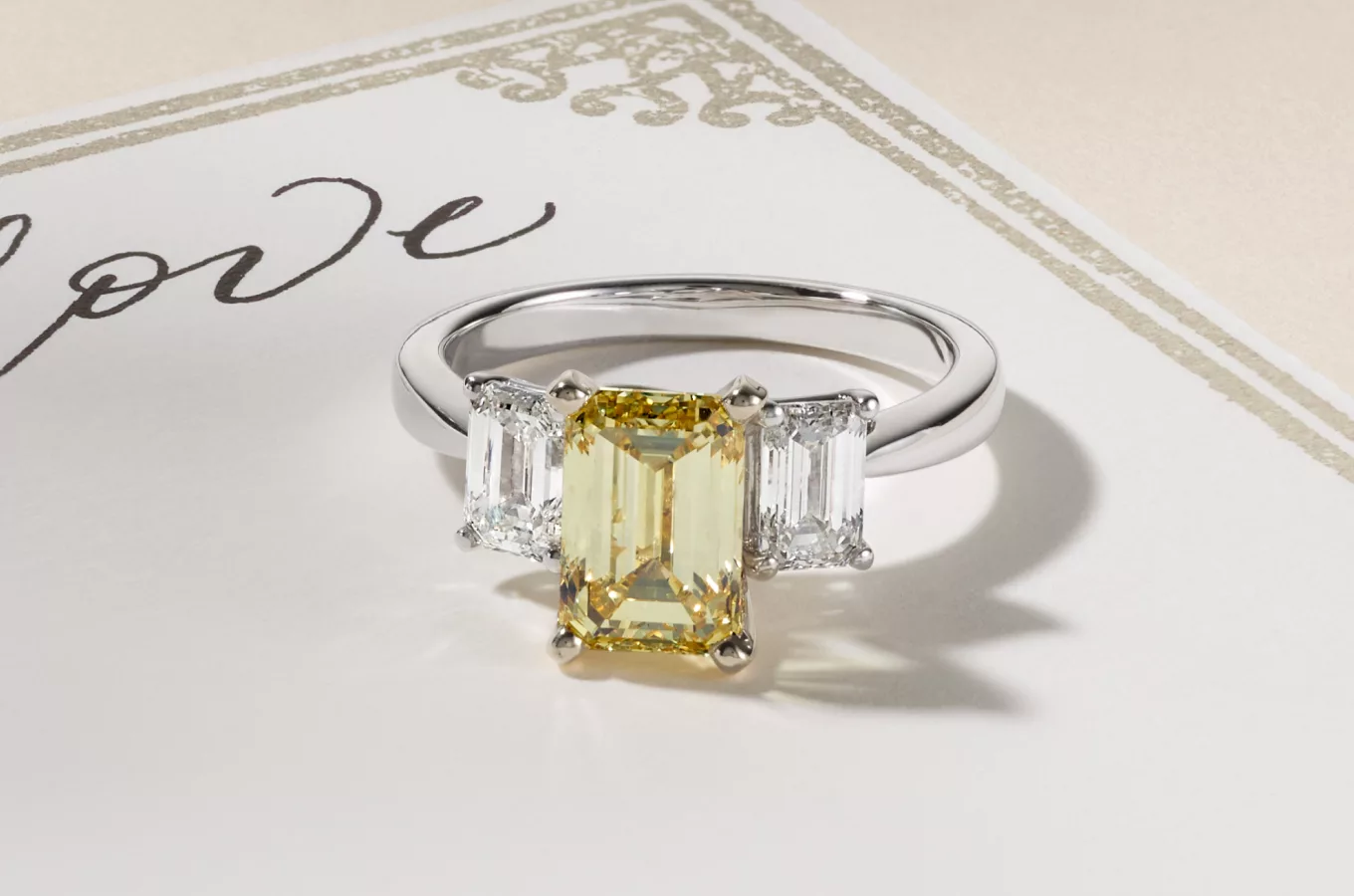 An Emerald cut Fancy Yellow Lab-grown diamond set in a three stone engagement ring with diamonds in a white gold ring