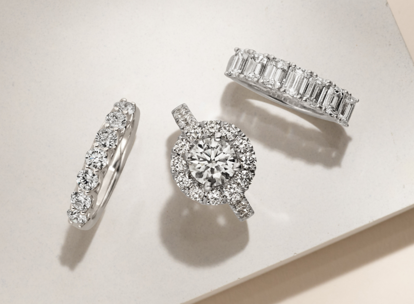 Matching wedding ring set featuring round diamond center stone in a white gold halo setting. With matching wedding band options featuring emerald cut diamonds or round cut diamonds