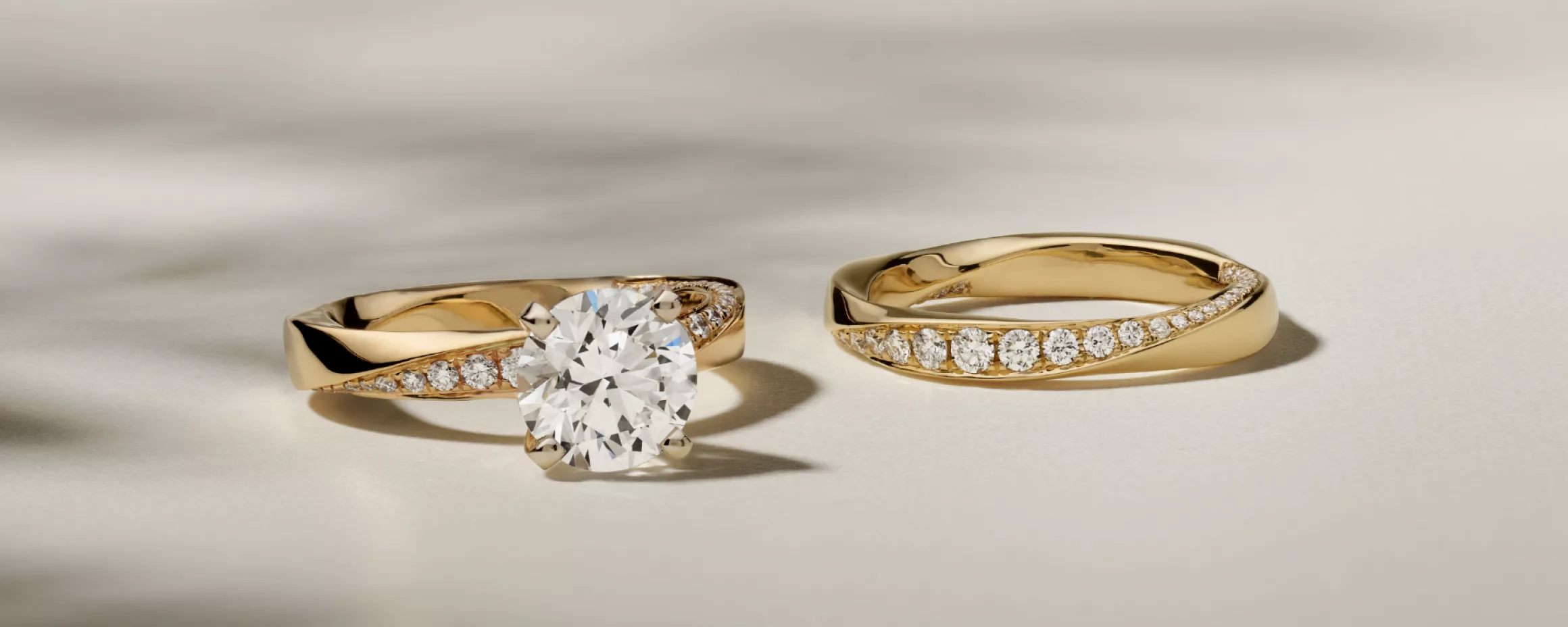 Matching wedding ring set featuring around diamond center stone in yellow gold. Twisting diamond pattern on an engagement ring and matching wedding band set
