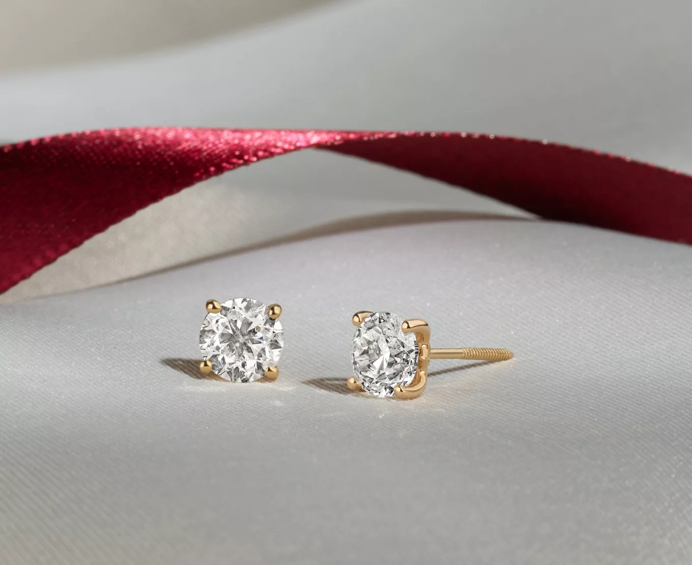 diamond stud earrings with a red ribbon behind them