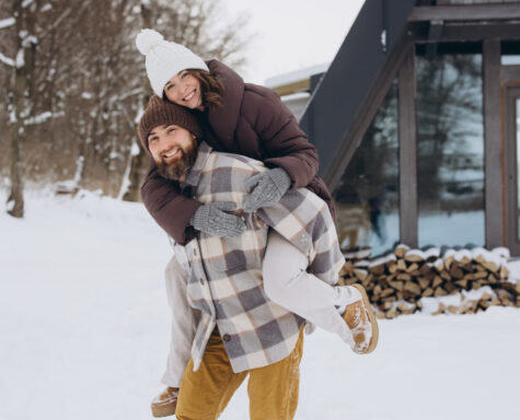 A couple outside in front of a snowy cabin