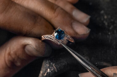 jeweler setting a blue center stone into a gold engagement ring