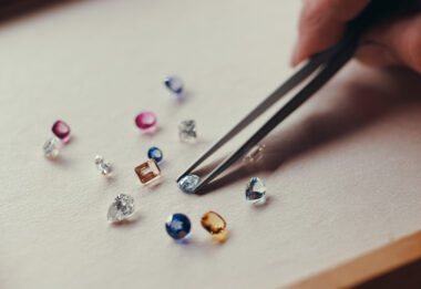assorted loose gemstones and diamonds, a jeweler is selecting one with a pair of tweezers