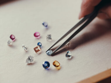 assorted loose gemstones and diamonds, a jeweler is selecting one with a pair of tweezers