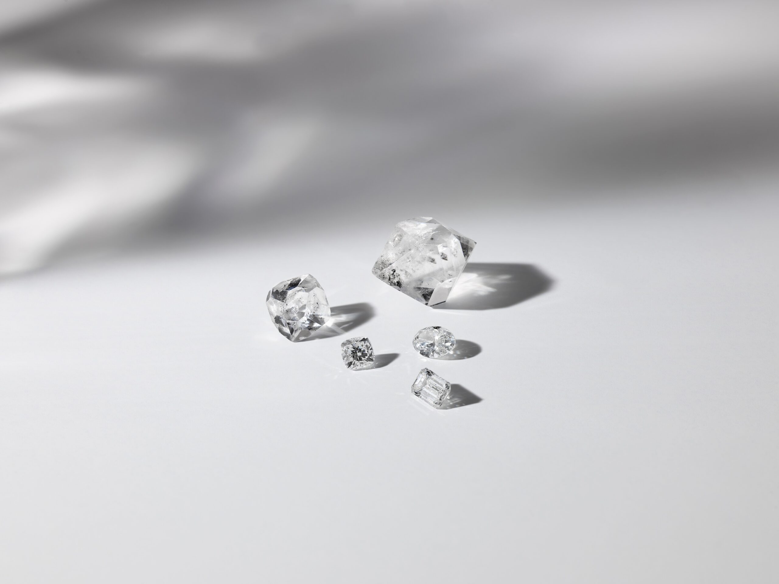 image of rough diamonds and three cut diamonds: emerald cut, oval cut, and cushion cut