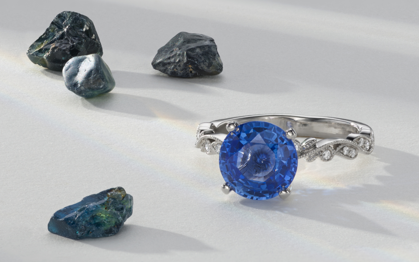 blue sapphire engagement ring with raw gemstones in the background