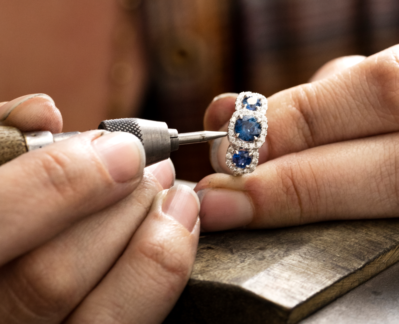Haley a jeweler at Shane Co., close up of her hands holding a white gold ring featuring 3 blue sapphire surrounded by diamonds