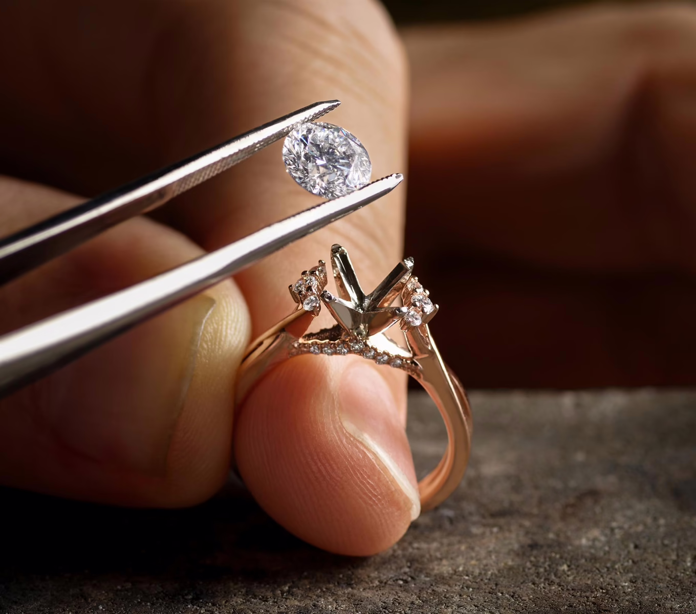 The image captures a close-up moment of a jeweler's hands working on a ring. The jeweler is using a pair of tweezers to carefully place a large, oval-shaped clear gemstone, likely a diamond, into an empty setting on the ring. The ring itself has a detailed design with smaller gemstones already set into the band and the prongs that are ready to hold the main stone. The background is out of focus, drawing attention to the intricate work being done on the ring. The lighting highlights the sparkle of the diamond and the shine of the metal, emphasizing the craftsmanship involved in setting the gemstone. The image conveys a sense of precision and meticulous attention to detail, typical of fine jewelry making or repair.