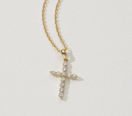 Leonie 0.20 tcw Diamond Cross Pendant The image features a beautiful gold necklace with a cross pendant adorned with clear gemstones, likely diamonds. Chain: The chain is made of gold, featuring a delicate and elegant link pattern that complements the pendant. Pendant: The pendant is a cross shape, crafted from gold and encrusted with a series of round, clear gemstones. Each arm of the cross is studded with diamonds, creating a sparkling and radiant effect. The simplicity of the design allows the brilliance of the gemstones to stand out, making the pendant a striking focal point. The background is plain and light-colored, which helps to highlight the necklace and its details. The overall presentation emphasizes the elegance and craftsmanship of the jewelry, showcasing the pendant's delicate design and the sparkle of the gemstones. This piece combines classic religious symbolism with luxurious materials, making it suitable for both everyday wear and special occasions.